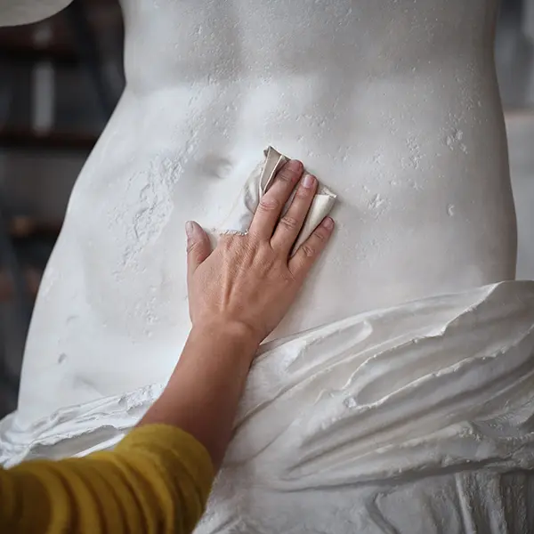 A close-up of our artisan’s hand applying a patina with a cloth on the torso of the Venus de Milo