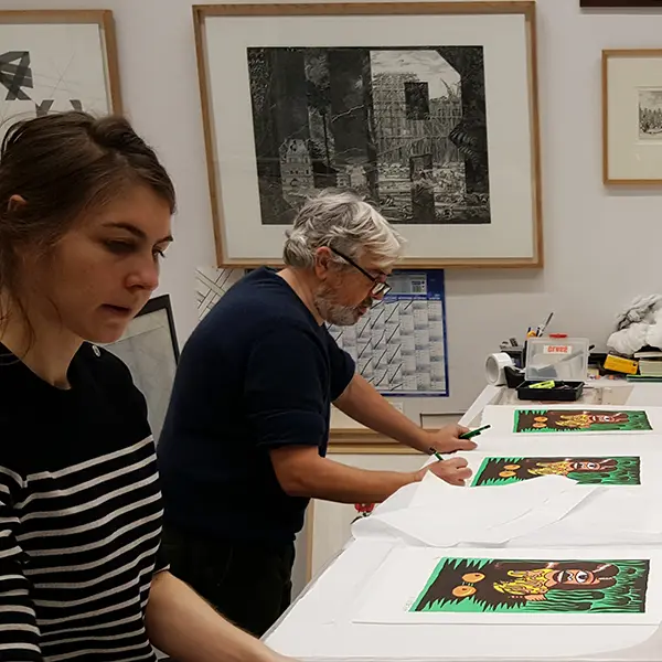 Prise de vue dans l’atelier de chalcographie. Hervé Di Rosa signe les tirages de Renée des Îles. On voit dans le champ Lucile, notre imprimeur taille-doucier qui a travaillé avec lui sur cette estampe. Au mur sont affichées estampes de : Cyprien Gaillard, Jenny Holzer, François Morellet, Louise Bourgeois