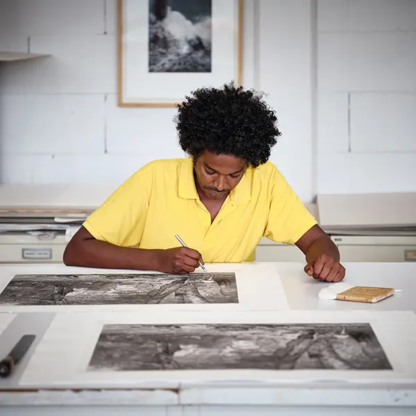 A shot in the Chalcographie du Louvre workshop. Our artisan is sitting and doing the final touch-ups on a print. On the wall, two contemporary prints are displayedPrise de vue dans l'atelier de chalcographie. Notre artisan est assis et fait des dernières retouches sur une estampe. Au mur sont affichées deux estampes contemporaines