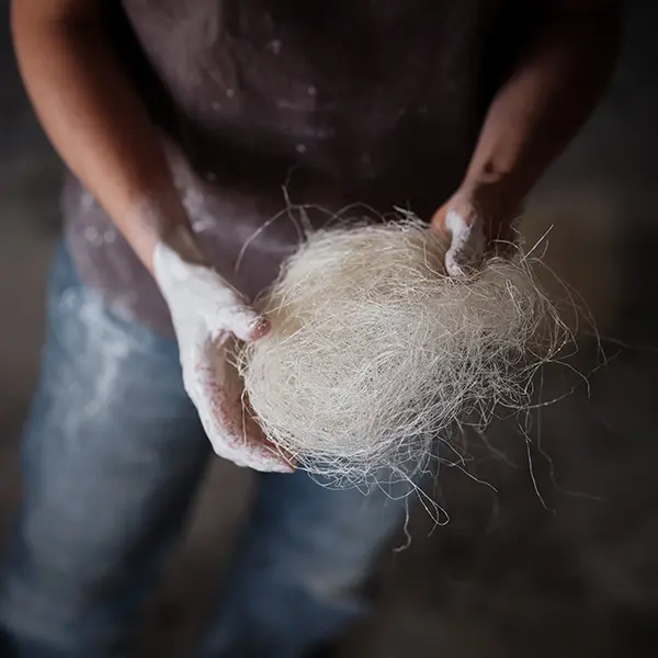 Gros plan sur les main blanches de plâtre de notre artisan qui tient une boule de fibres naturelles