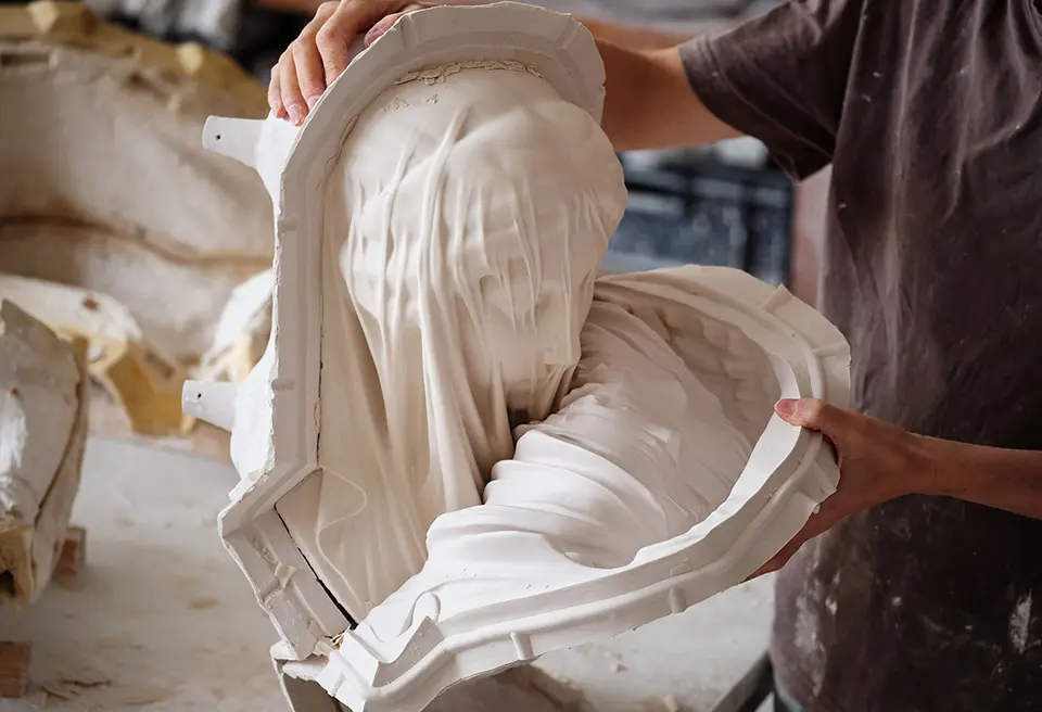 Gros plan sur le geste d'un artisant en train de démouler la reproduction de la Vierge voilée de Giovanni Strazza (ref:PI007386)